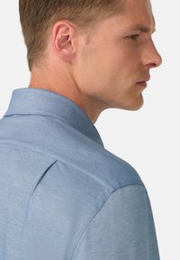 Camicia azzurro chiaro con colletto, caratterizzata da un tessuto testurizzato, una piega sul retro e cuciture lisce. Il design è pensato per una vestibilità aderente.