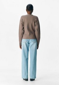 Brun strikket sweater med rund hals, parret med lys blå lige ben jeans. Outfittet har en afslappet pasform og minimal detaljer.