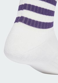 Calcetín blanco con rayas moradas, con un puño acanalado y textura suave, destacando un claro contraste de colores y un ajuste ceñido.