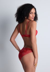 Soutien-gorge en dentelle rouge et culotte transparente assortie avec broderie florale, dotés de bretelles ajustables et d'une fermeture au dos. Fini lisse et détails délicats.