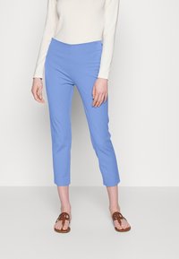 Ljusblå korta byxor med en mjuk textur och elastisk midja, i kombination med bruna platta sandaler. Modell som bär en långärmad topp.