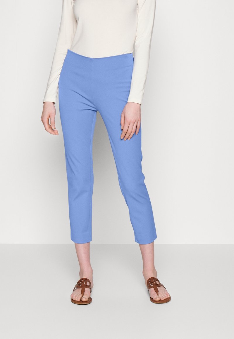 Ljusblå korta byxor med en mjuk textur och elastisk midja, i kombination med bruna platta sandaler. Modell som bär en långärmad topp.