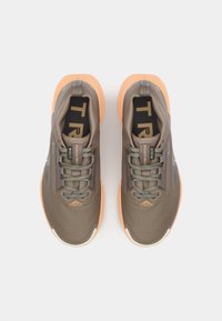 Men's running shoes in dark brown with mesh panels, laces in teal, and orange rubber soles. Features a logo on the tongue and side accents.