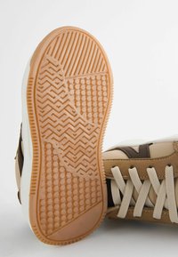 Baskets beiges et marron avec une semelle en gomme texturée, des détails sur la tige et des lacets beiges. Fabriquées dans un mélange de matériaux, y compris du daim et du cuir.
