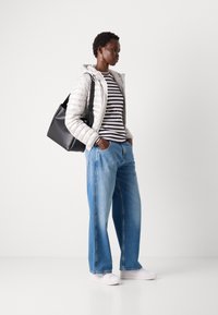 Lichtgrijze pufferjack, zwart gestreept shirt met lange mouwen, blauwe wijde jeans, witte sneakers en een zwarte totebag. Eenvoudig en modern ontwerp.