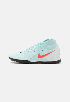 Hellblauer hoher Fußballschuh mit leuchtend rotem Nike-Swoosh, schwarzer, strukturierter Sohle und Schnürsenkeln, speziell für Kunstrasen entwickelt.