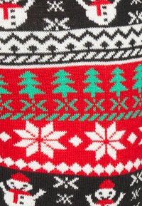 Pull en tricot avec des motifs de bonhommes de neige, de sapins de Noël et de flocons de neige rouges, verts et blancs sur un fond noir.