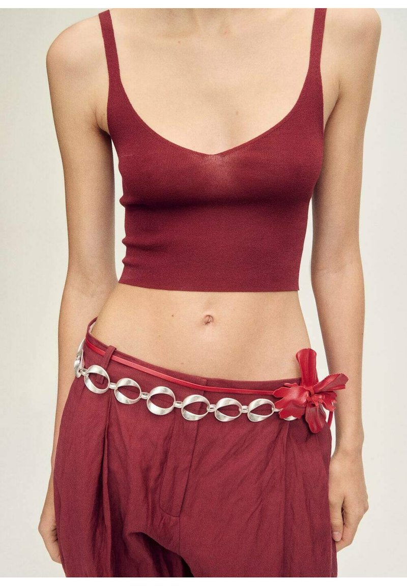 Bordová kr cropped top s tenkými ramínky, v kombinaci s volnými bordovými kalhotami, doplněný stříbrným kruhovým páskem a kontrastním červeným květinovým akcentem.