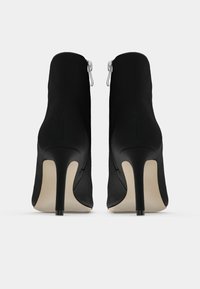 Botines negros de tacón alto con textura suave, que cuentan con cremalleras laterales y punta afilada. Tacón de aguja, diseño limpio y minimalista.