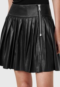 Falda plisada de cuero negro con una cintura alta, que presenta un detalle de cremallera plateada en el lateral y una textura suave y brillante.
