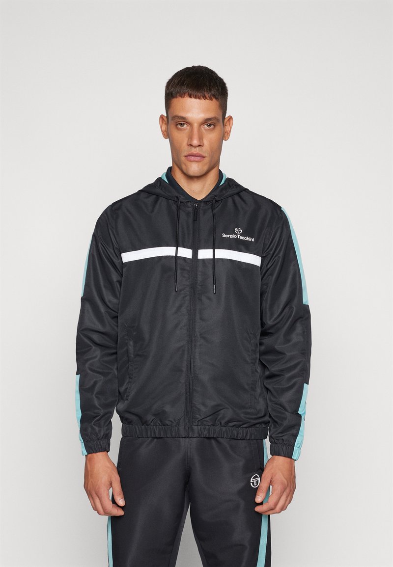 Chaqueta negra con cremallera y capucha, con detalles en blanco y verde azulado, puños elásticos y un logo en el pecho. Tela suave con un diseño deportivo.
