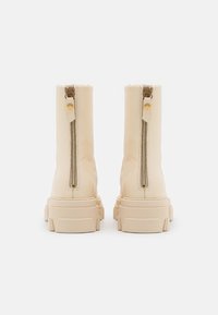 Beige Leder-Ankle-Boots mit einer klobigen Sohle, seitlichen Reißverschlüssen, strukturiertem Finish und goldfarbenen Hardwaredetails.