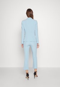 Lichtblauw pak met getailleerd jasje en cropped broek, gemaakt van gladde stof. Zwarte hoge hakken maken de look compleet.