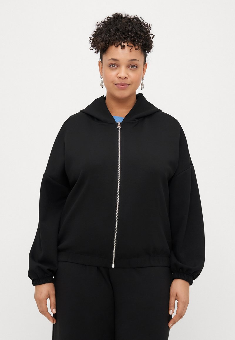 Svart zip-up hettegenser med snorhette, lange ermer og elastiske mansjetter. Myk stoff med en avslappet passform og minimalistisk design.