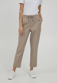 Beige neplederen joggerbroeken met een elastische tailleband, koord en zijzakken. Vaak afgebouwde broekspijpen met gestikte details.