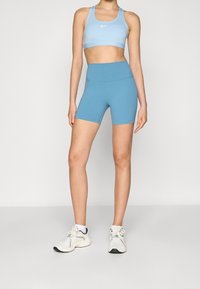 Jasnoniebieski sportowy biustonosz i dopasowane szorty z wysokim stanem z miękkiego, elastycznego materiału. Biały detal z logo na biustonoszu. Białe sneakersy z akcentami.