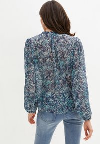 Blouse à motif floral dans des tons de bleu et de vert, avec des manches bouffantes, un col froncé et une taille cintrée. Confectionnée en tissu léger.