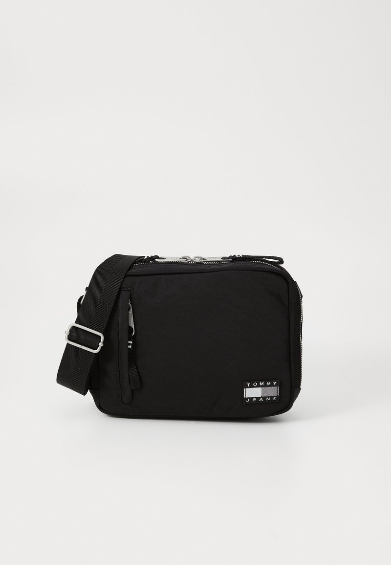 Sort nylon crossbody taske med lynlåslukning, justerbar rem og et logo-patch. Rektangulær form, glat tekstur.