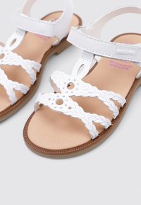 Sandalias blancas con tiras trenzadas, cerradas en el medio, con recortes decorativos y acentos de strass. Suela marrón, plantilla suave.