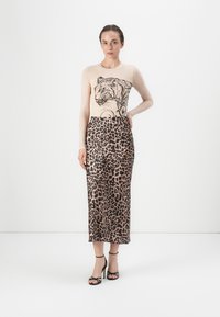 Beige langharige top met een zwart tijger graphic en een lederen high-waisted rok met luipaardprint. Model draagt zwarte strap heels.