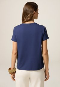 Marineblaue Baumwoll-T-Shirt mit kurzen, aufgerollten Ärmeln, Rundhalsausschnitt und lässiger Passform, getragen mit cremefarbenen Hosen.