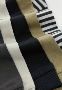 Quatre chaussettes tricotées pliées en noir uni, beige et à rayures noir et blanc, disposées côte à côte sur une surface blanche.