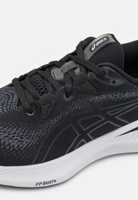 Scarpa sportiva nera con tomaia texturizzata, dettagli grigi, suola imbottita e logo del marchio. I lacci e i fori per i lacci migliorano la regolabilità.