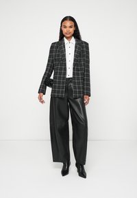 Crno-bijeli karirani sako s oštrim reverima, uparen s visokim crnim kožnim širokim hlačama i šiljastim crnim gležnjačama.