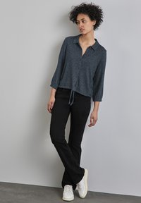 Mörkgrå blus med krage och 3/4-ärmar, knytning i midjan. Tillsammans med svarta raka jeans och Vita sneakers. Slät textur.