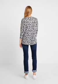 Haut à motif léopard en noir et gris, manches trois-quarts, col rond, associé à un jean bleu foncé et des baskets blanches.