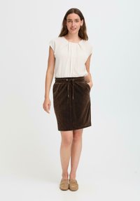 Jupe en velours côtelé marron avec taille à cordon, poches latérales et design mi-long, associée à un chemisier à manches courtes beige clair.