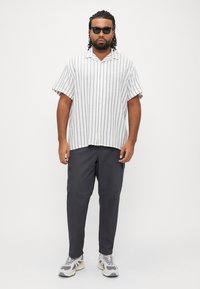 Ριγέ κοντομάνικο πουκάμισο σε λευκό και ανοιχτό γκρι, συνδυασμένο με σκούρο παντελόνι cargo. Αξεσουάρ περιλαμβάνουν μαύρα γυαλιά ηλίου και γκρι αθλητικά παπούτσια.