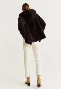 Sort faux fur frakke med hætte, oversized pasform, tætsiddende ærmer, båret med hvide jeans og støvler med slangeskindsprint.