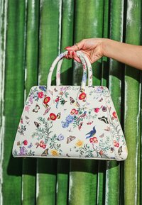 Borsa bianca con motivi floreali e farfalle, caratterizzata da una forma strutturata, manici doppi e un materiale liscio.