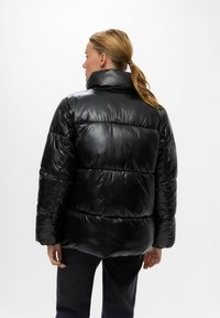 Doudoune noire avec une finition brillante et matelassée, col haut et coupe ample. Présente des manches larges et une texture lisse.