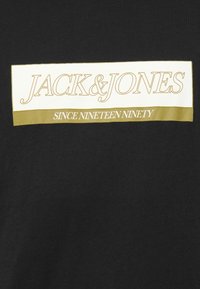 Fekete szövet, fehér és olíva zöld téglalap alakú címkével, amelyen a "JACK & JONES" és a "SINCE NINETEEN NINETY" felirat olvasható.