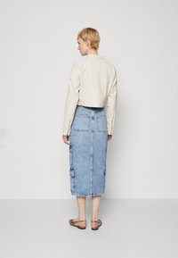 Veste courte en cuir crème associée à une jupe en denim bleu clair de mi-longueur avec des poches cargo et un ourlet brut.
