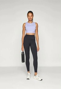 Lila sportmellény, magas derekú fekete leggings, fekete víz kulacs és fehér sportcipő; sima, testhez álló dizájn, minimalista márkázás.