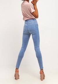 Jeans skinny taille haute, bleu clair, avec une texture lisse, dotés de poches arrière et d'un léger extensibilité. Associé à un t-shirt rose.