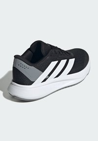 Scarpa sportiva nera con accenti bianchi, tomaia in mesh testurizzato, suola spessa bianca e dettaglio grigio sul tallone con fori per la ventilazione.