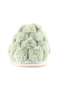 Pantofole verdi in peluche con una superficie texturizzata e soffice. Presentano un design a incrocio in materiale morbido e una suola piatta di colore chiaro.