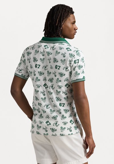 Camisa polo blanca con patrones de hojas verdes y logotipos. Presenta un collar verde y mangas acanaladas. La tela parece texturizada y tiene un ajuste regular.
