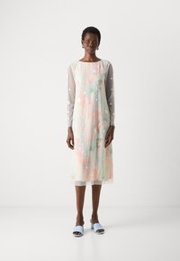 Licht, bloemenprint jurk met lange, doorschijnende grijze mouwen versierd met witte accenten. De zoom valt tot halverwege de kuit, gecombineerd met lichtblauwe instappers.