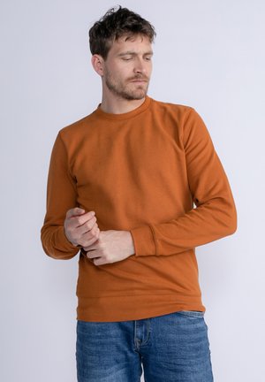 Sudadera naranja de mezcla de algodón, con mangas largas, cuello redondo y puños acanalados. Combinada con jeans de mezclilla azules.