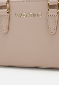 Valentino gaiši rozā rokassoma ar teksturētu sintētisko materiālu, zelta detaļām, divām siksnām un iegravētu logotipu priekšpusē.