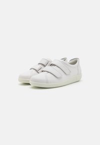 White, low-top sneakers made of textured leather with dual Velcro straps. Rounded toe and a soft, flexible rubber sole. Minimal design.