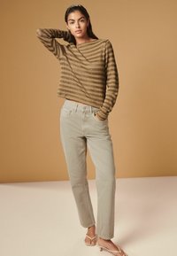 Langærmet top med brune og beige striber, parret med lys beige lige bukser og beige sandaler mod en varm baggrund.