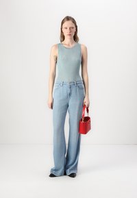 Débardeur côtelé bleu clair, jeans évasés en denim clair taille haute et petit sac à main rouge. Le modèle se tient devant un fond neutre.