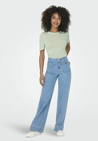 Top verde chiaro a maniche corte con una vestibilità morbida, abbinato a jeans in denim blu a vita alta e gamba larga, con hardware dorato e grandi tasche.