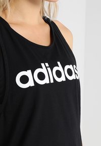 Czarny top na ramiączkach wykonany z bawełny, z dużym białym logo "adidas" na przodzie. Okrągły dekolt i bezrękawnik.